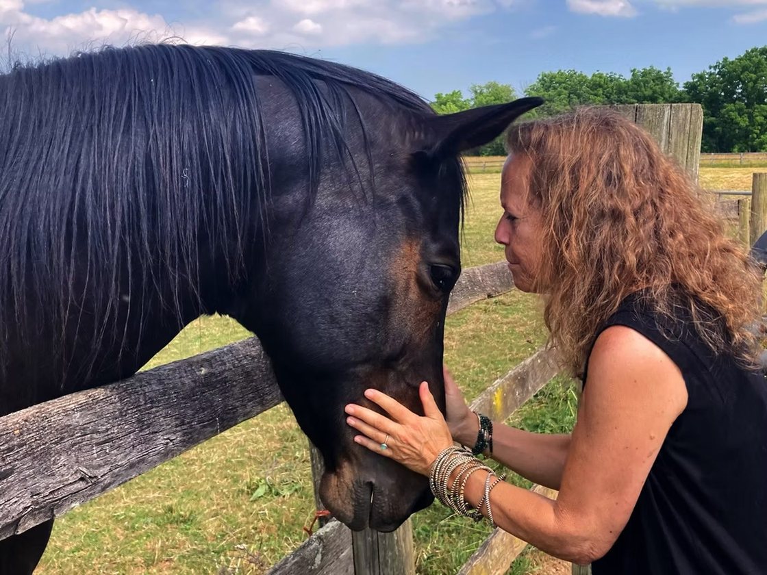 Donna Sue Rosenthal forehead to forehead with a horse in a field